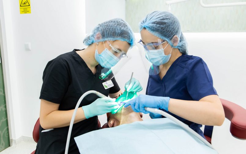 Medici si pacient in cabinetul stomatologic in timpul unei proceduri de albire dentară cu laser