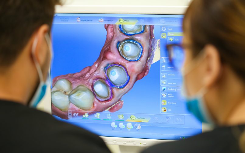 Medici care privesc un monitor ce indica tehnologia pentru lucrările dentare