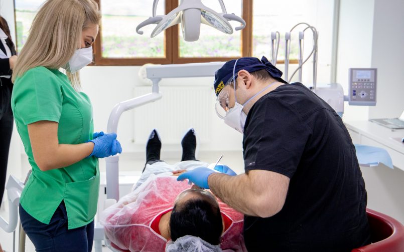 medic dentist in dreapta si asistenta in stanga scaunul stomatologic in timpul unui consult pentru eliminarea tartrului dentar