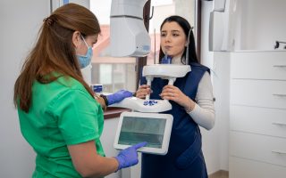 femeie care realizeaza un tip de radiografie dentara si asistenta care seteaza aparatura digitala