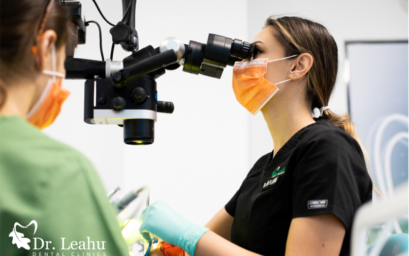 asistent in stanga, microscop dentar in mijloc, medic stomatolog in dreapta efectuează un tratament endodontic la microscop