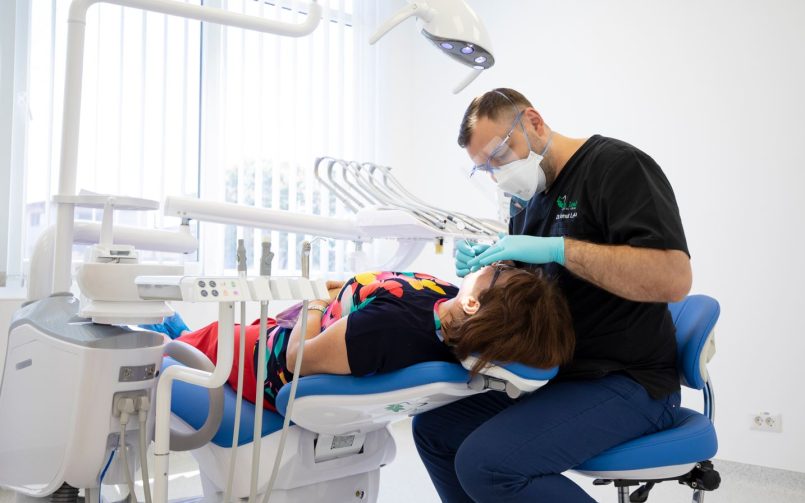 Medic stomatolog in dreapta, pacient pe scaunul stomatologic in cabinetul de medicina dentara