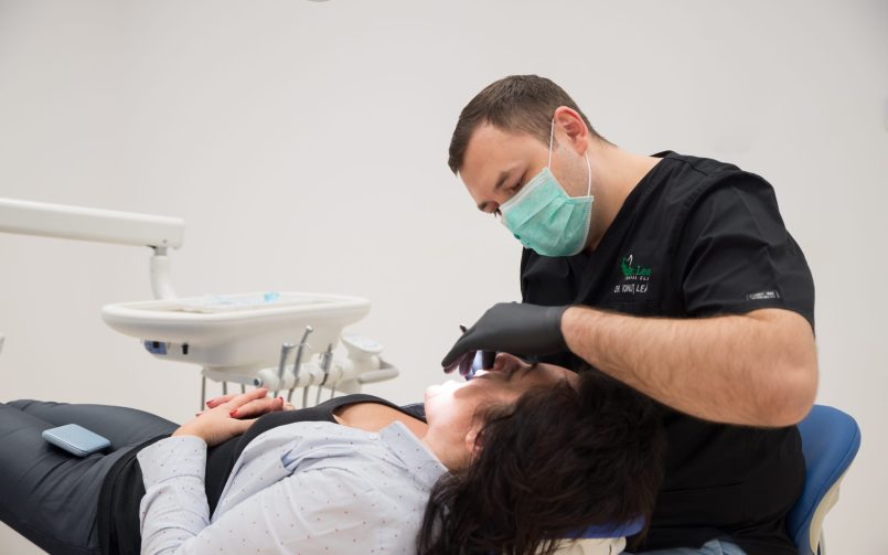 Medic stomatolog in dreapta, pacient pe scaunul stomatolog in cabinetul dentar