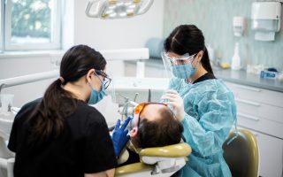 medic stomatolog in dreapta, asistent medical in stanga, pacient pe scaun in cabinetul de medicina dentara